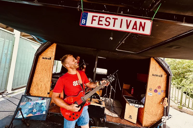 un homme jouant de la guitare devant le panneau festi'van